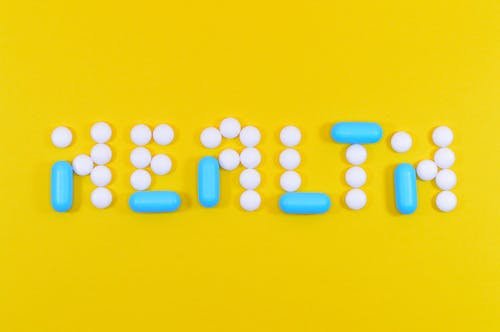 Free Pills spelling 'health' on a vibrant yellow background, symbolizing wellness. Stock Photo